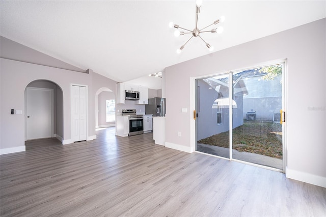 unfurnished living room with a chandelier, arched walkways, light wood-style floors, and vaulted ceiling