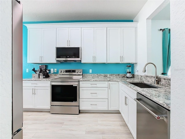 kitchen with light stone counters, stainless steel appliances, wood tiled floor, white cabinetry, and a sink