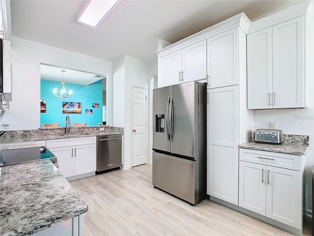 kitchen with decorative light fixtures, appliances with stainless steel finishes, white cabinetry, a sink, and light wood-type flooring