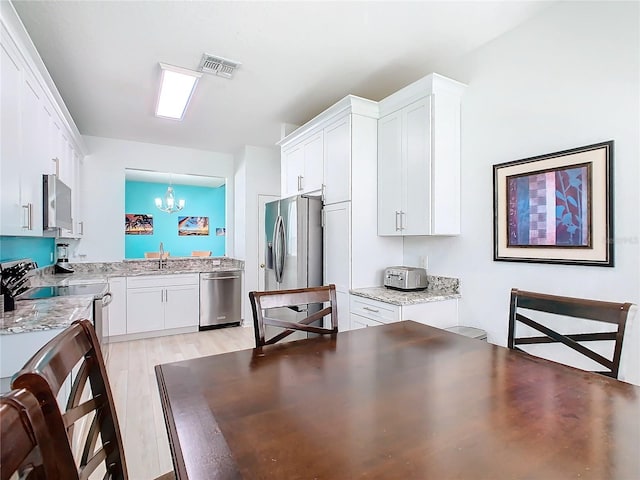 kitchen featuring stainless steel appliances, a sink, visible vents, white cabinets, and decorative light fixtures