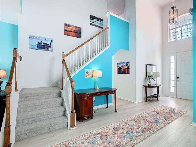 foyer entrance with a notable chandelier, a towering ceiling, light wood-style floors, baseboards, and stairs