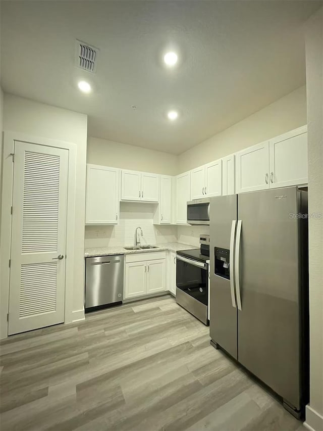 kitchen featuring appliances with stainless steel finishes, sink, light wood-type flooring, white cabinetry, and light stone countertops