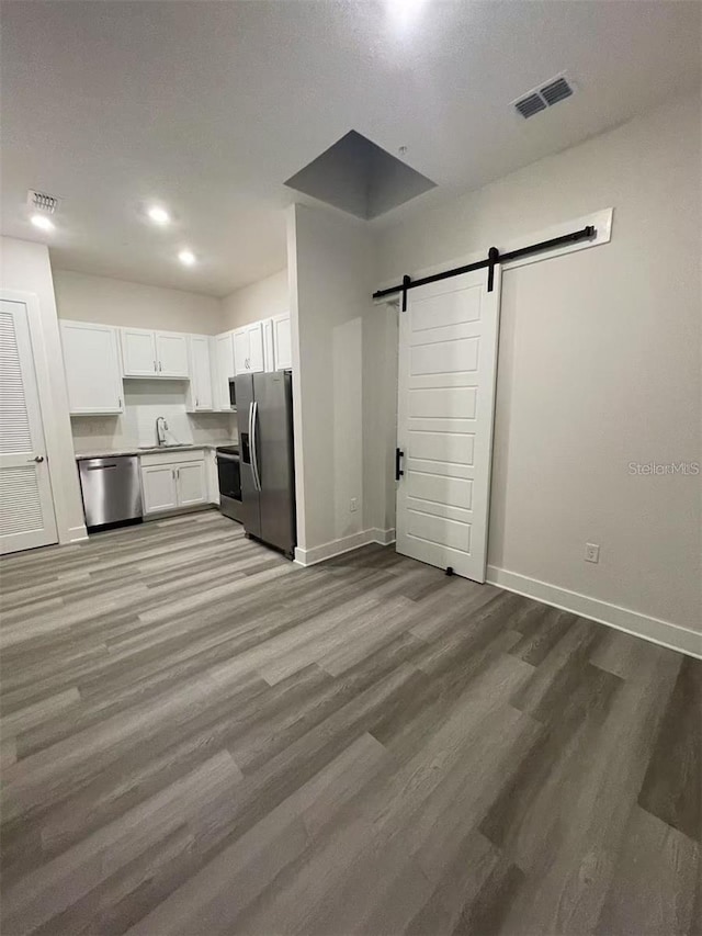 kitchen featuring a barn door, light wood-type flooring, stainless steel appliances, and white cabinets