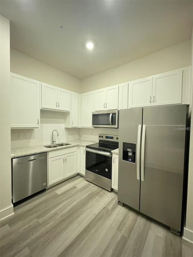 kitchen featuring stainless steel appliances, light stone countertops, light hardwood / wood-style floors, sink, and white cabinetry