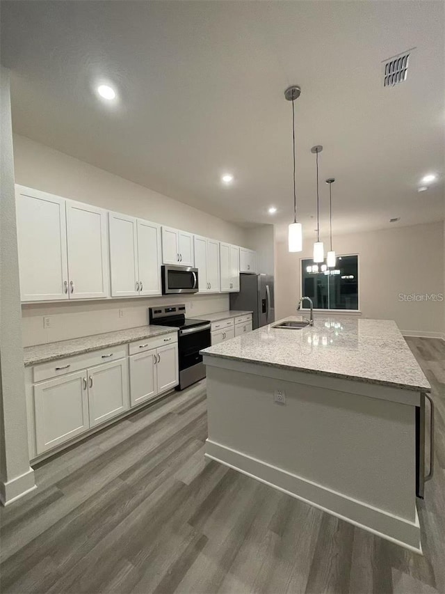 kitchen with appliances with stainless steel finishes, decorative light fixtures, white cabinets, light stone countertops, and a kitchen island with sink