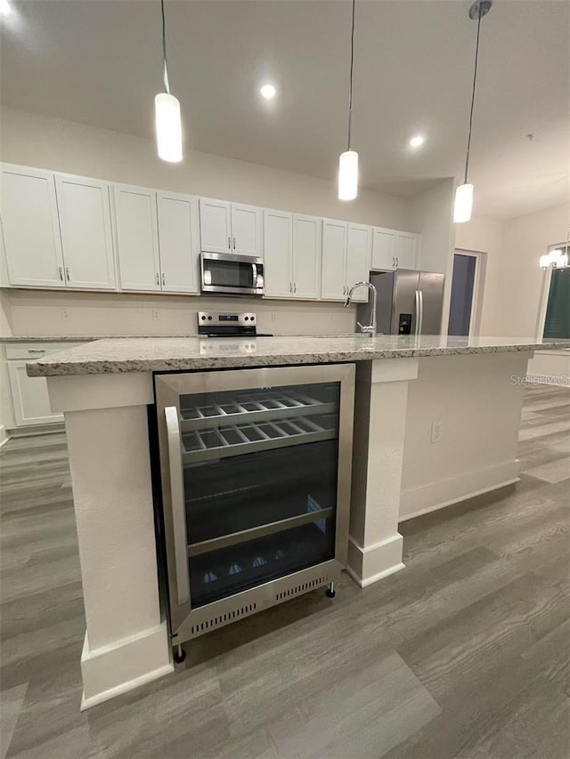 kitchen featuring white cabinetry, beverage cooler, stainless steel appliances, and an island with sink