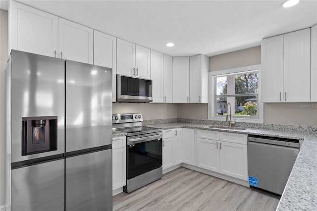 kitchen with appliances with stainless steel finishes, white cabinets, a sink, and light wood-style flooring