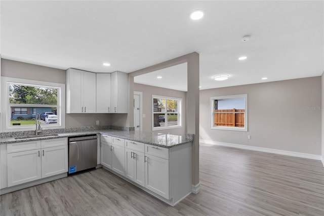 kitchen featuring white cabinetry, a sink, stainless steel dishwasher, and light stone countertops