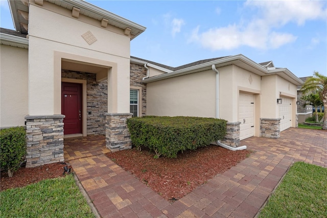 view of exterior entry with a garage, stone siding, decorative driveway, and stucco siding