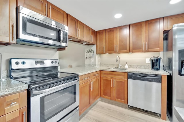 kitchen featuring light wood-type flooring, stainless steel appliances, light stone counters, and sink