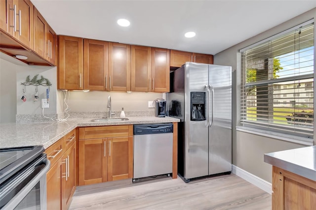 kitchen with light wood-type flooring, stainless steel appliances, light stone countertops, and sink