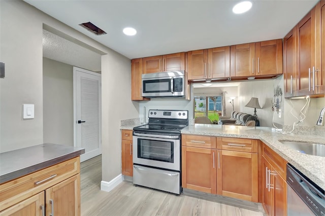 kitchen featuring light wood-type flooring, stainless steel appliances, light stone counters, sink, and kitchen peninsula