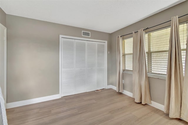 unfurnished bedroom featuring a textured ceiling, a closet, and light hardwood / wood-style flooring