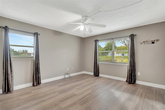 empty room with a textured ceiling, ceiling fan, light hardwood / wood-style floors, and plenty of natural light