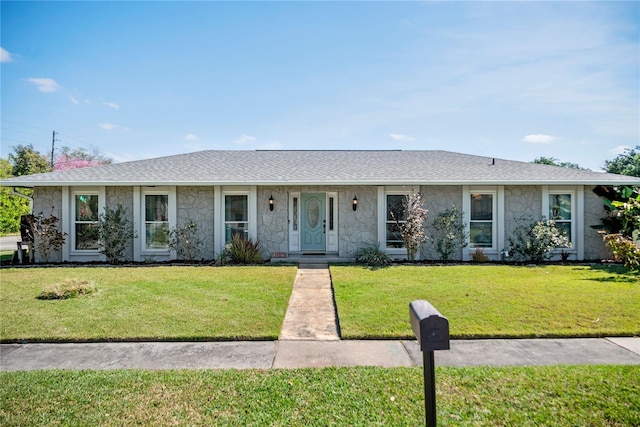 ranch-style home featuring a shingled roof, stone siding, and a front lawn