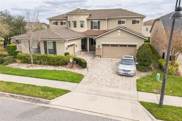 view of front facade featuring a garage, decorative driveway, stone siding, and stucco siding