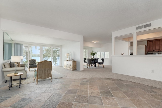 living room featuring light carpet, a textured ceiling, plenty of natural light, and visible vents