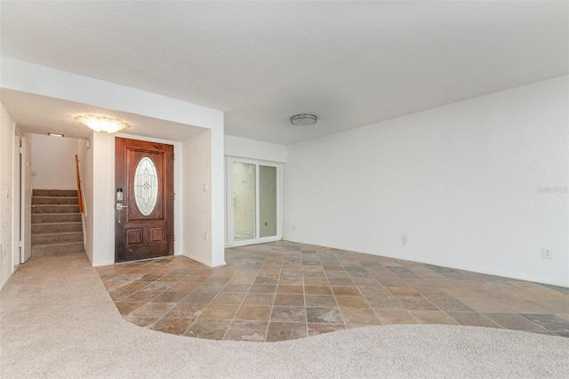 carpeted foyer entrance with stairs, stone finish floor, and a textured ceiling