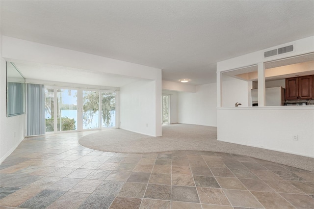 unfurnished room featuring a textured ceiling, stone finish flooring, light carpet, and visible vents