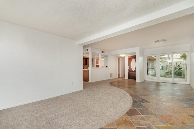 unfurnished living room featuring a textured ceiling, stone finish flooring, carpet, and visible vents