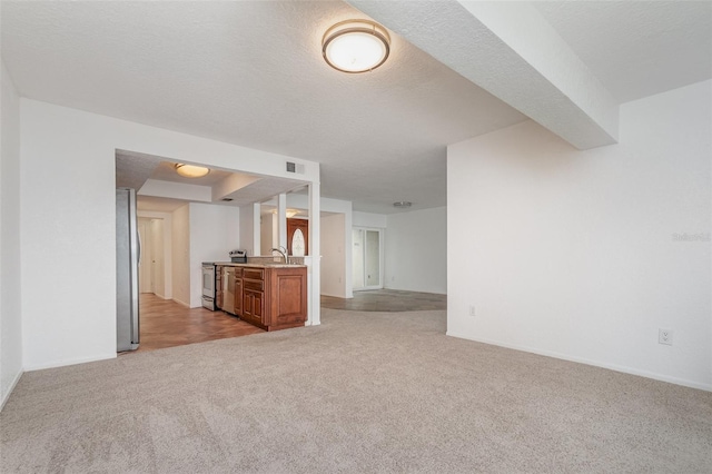 unfurnished living room with a textured ceiling, light carpet, a sink, visible vents, and baseboards