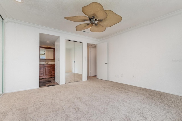 unfurnished bedroom featuring ensuite bathroom, a textured ceiling, ceiling fan, carpet floors, and crown molding