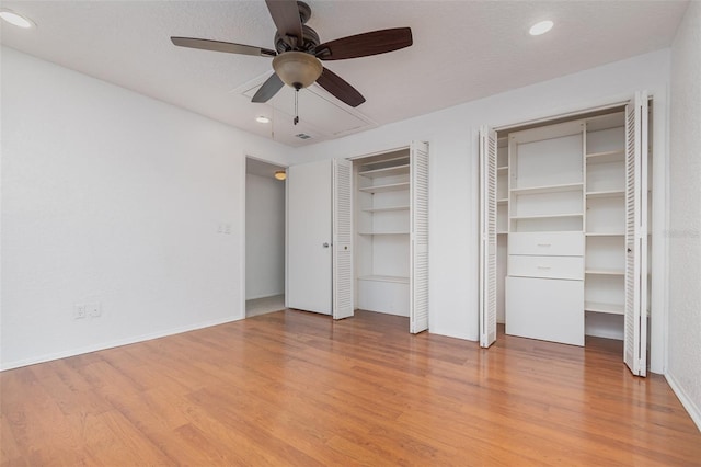 unfurnished bedroom featuring a textured ceiling, wood finished floors, two closets, and baseboards