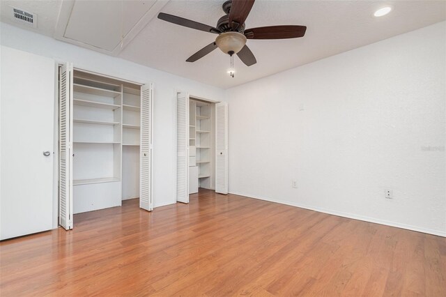 unfurnished bedroom featuring two closets, visible vents, attic access, a ceiling fan, and wood finished floors