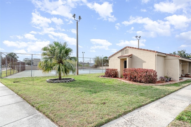 view of property's community with a tennis court, a lawn, and fence