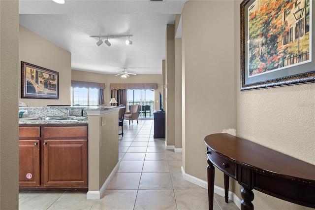 kitchen with a textured ceiling, ceiling fan, light tile patterned flooring, a sink, and light countertops