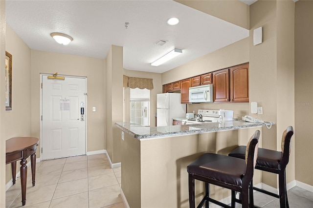 kitchen with white appliances, visible vents, light stone counters, a kitchen breakfast bar, and a peninsula