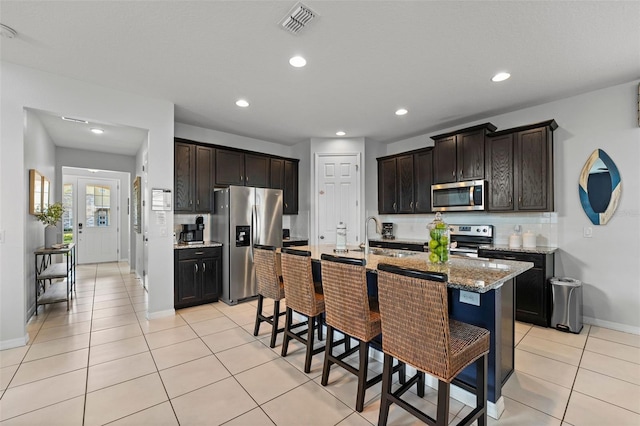 kitchen with appliances with stainless steel finishes, a kitchen breakfast bar, dark brown cabinetry, sink, and a kitchen island with sink