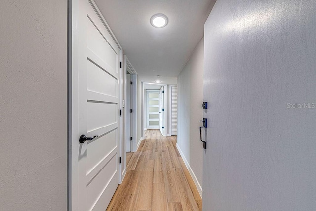 corridor with a textured wall, light wood-style flooring, and baseboards
