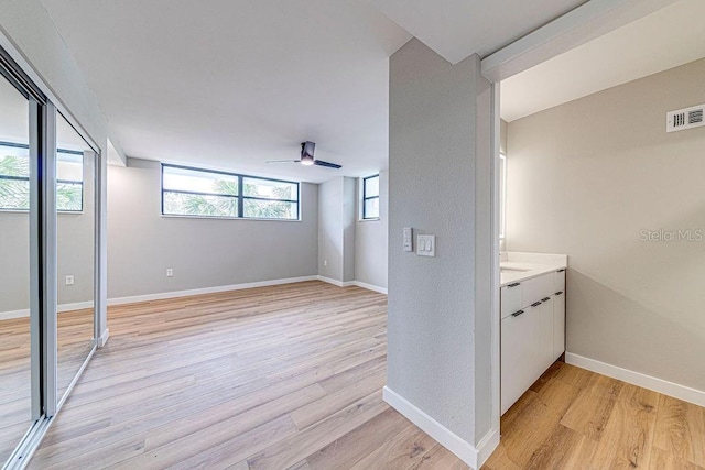 interior space featuring visible vents, ceiling fan, light wood-style flooring, and baseboards