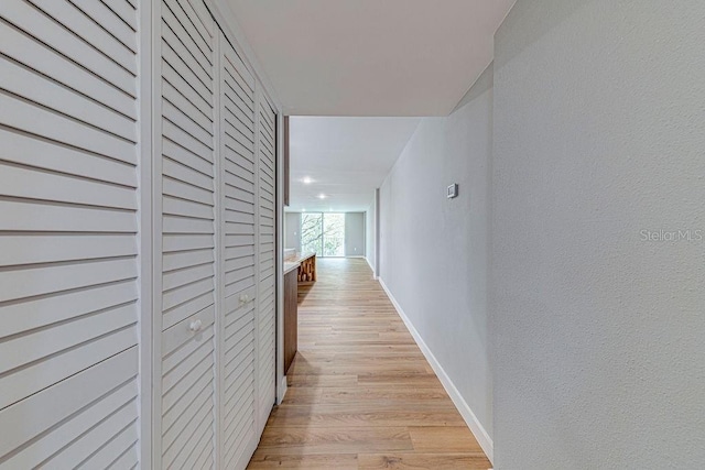 hall featuring a textured wall, light wood-style flooring, and baseboards