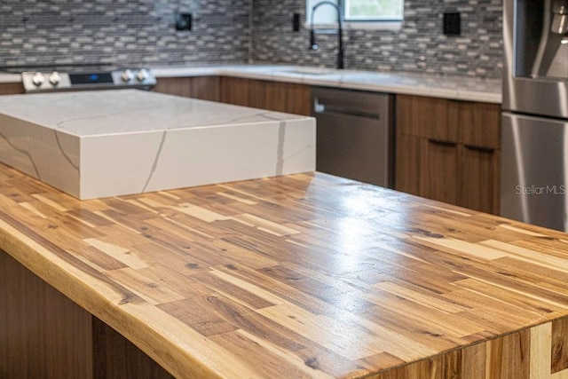 kitchen with butcher block counters, appliances with stainless steel finishes, tasteful backsplash, and wood finished floors