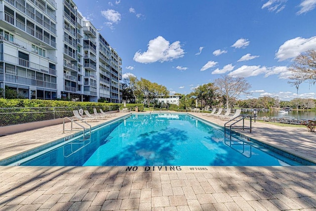pool featuring a water view, a patio area, and fence