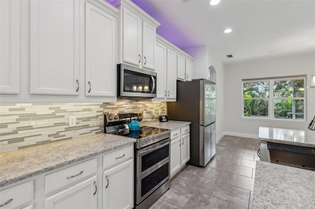 kitchen featuring appliances with stainless steel finishes, light stone counters, decorative backsplash, light tile patterned floors, and white cabinetry