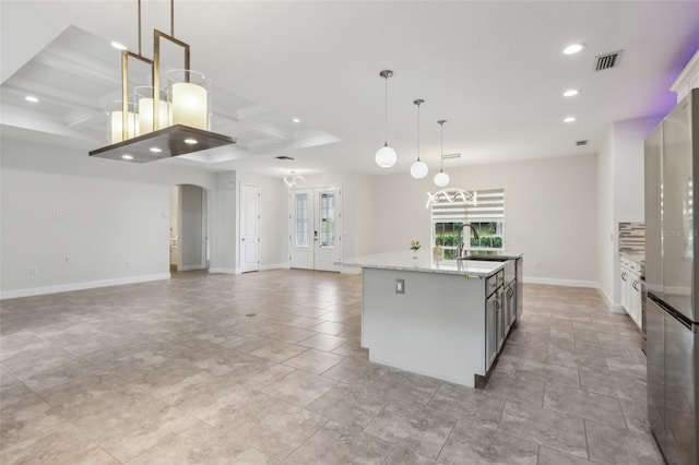 kitchen featuring an island with sink, white cabinetry, light stone countertops, and pendant lighting