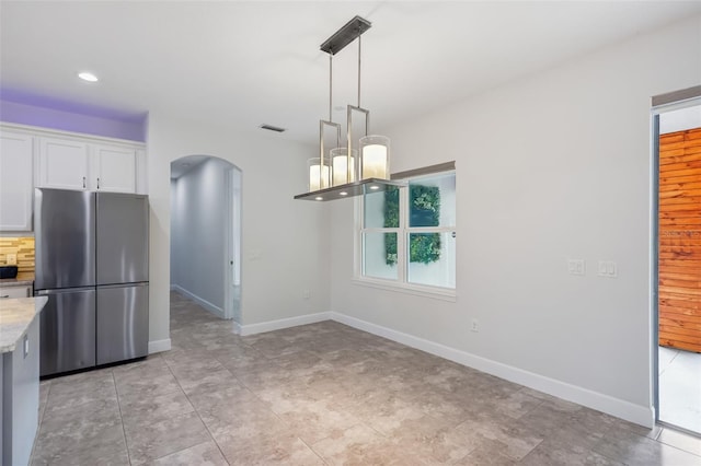 kitchen with white cabinets, light stone counters, pendant lighting, and stainless steel fridge