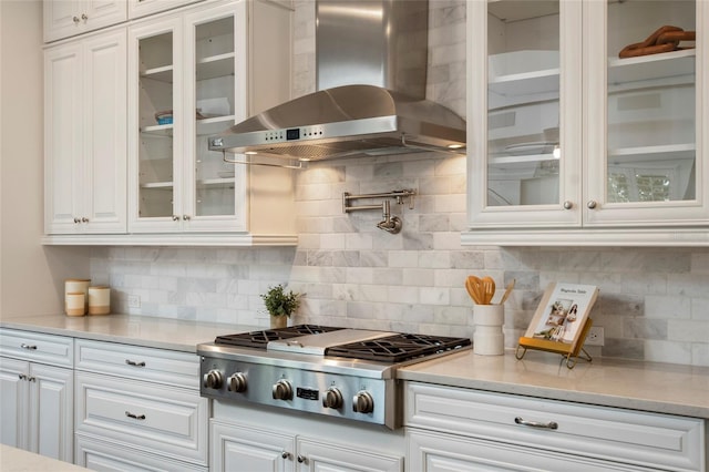 kitchen with tasteful backsplash, wall chimney range hood, white cabinets, stainless steel gas cooktop, and light countertops