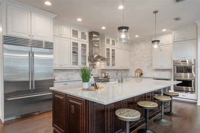 kitchen with stainless steel appliances, visible vents, wall chimney exhaust hood, and dark wood-style floors