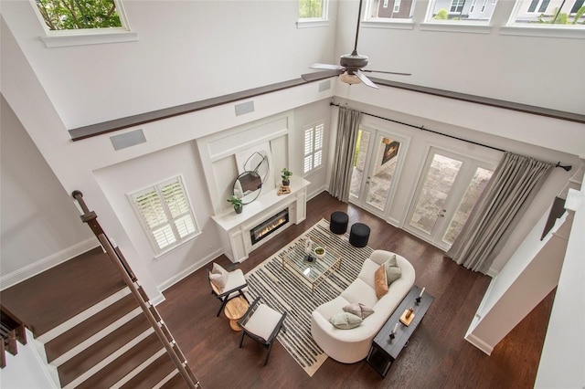 living room featuring visible vents, dark wood-style flooring, ceiling fan, a towering ceiling, and a glass covered fireplace
