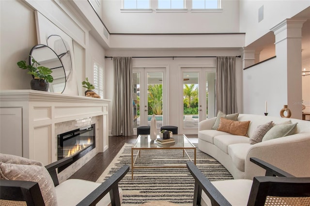 living area with a fireplace, a towering ceiling, dark wood-style flooring, and french doors