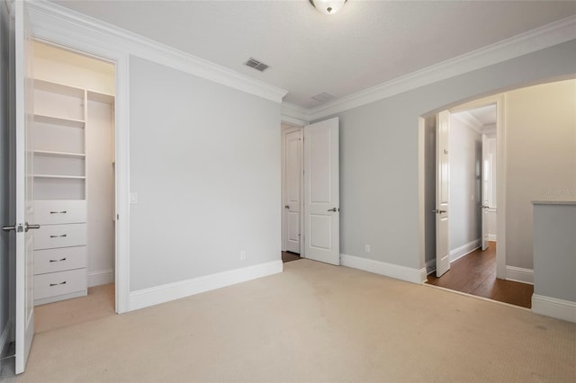 unfurnished bedroom featuring baseboards, crown molding, visible vents, arched walkways, and carpet