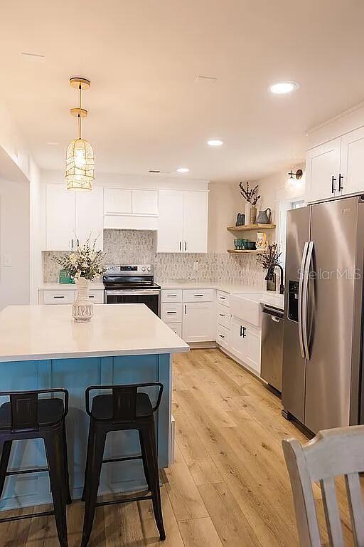 kitchen featuring pendant lighting, light hardwood / wood-style floors, stainless steel appliances, white cabinets, and decorative backsplash