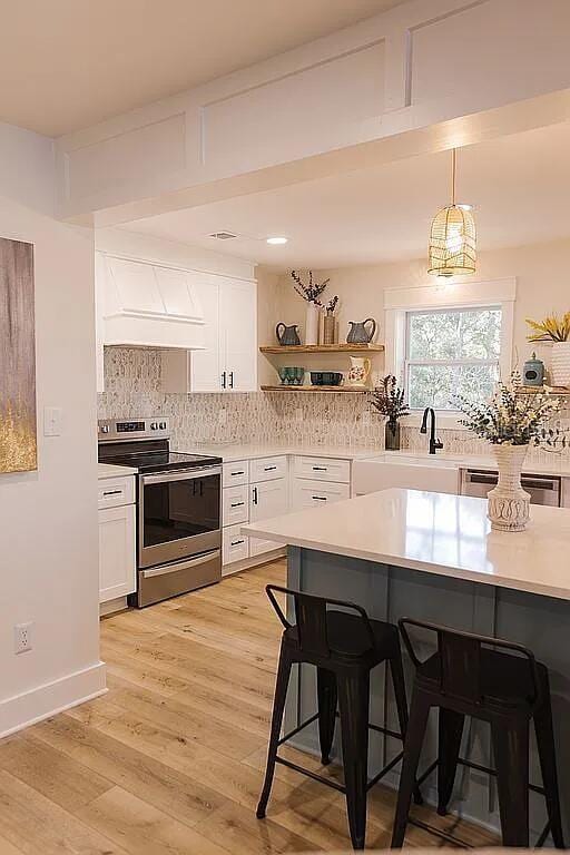 kitchen with white cabinets, stainless steel electric stove, a breakfast bar area, and decorative light fixtures