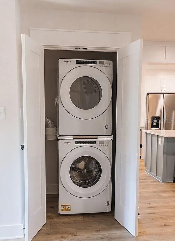 laundry room featuring stacked washer and clothes dryer and light hardwood / wood-style flooring