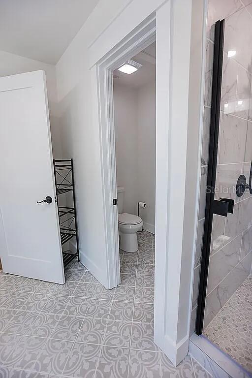 bathroom with tile patterned floors, a tile shower, and toilet