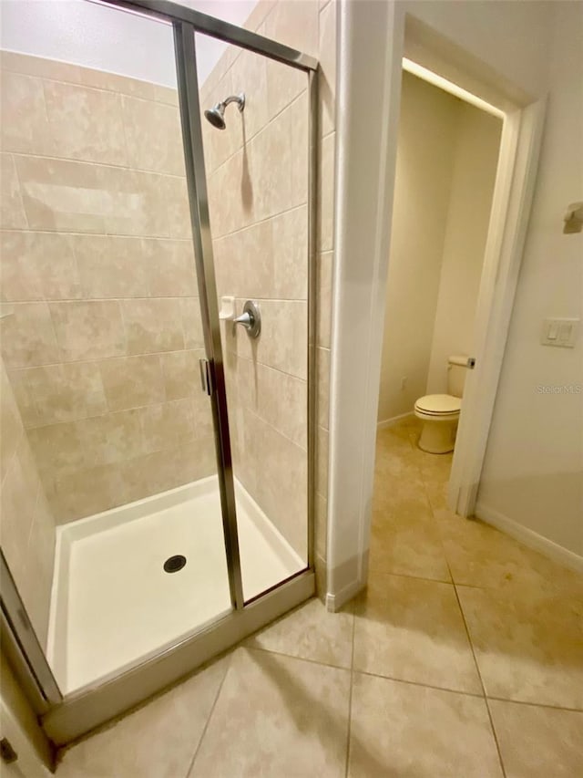 full bath with a stall shower, tile patterned flooring, baseboards, and toilet